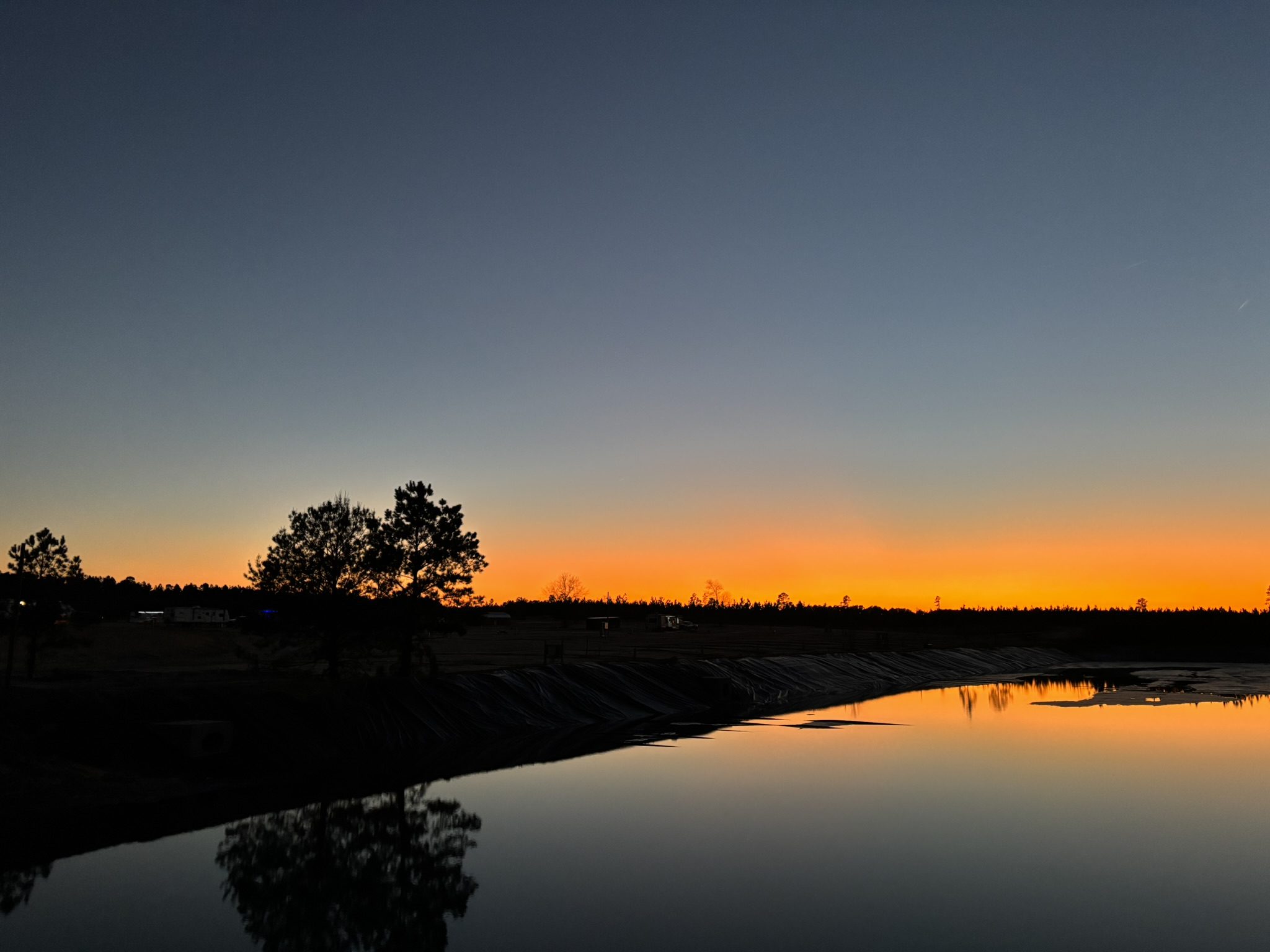A tranquil sunset reflecting on the calm waters of a pond at Standing Pines Campground.