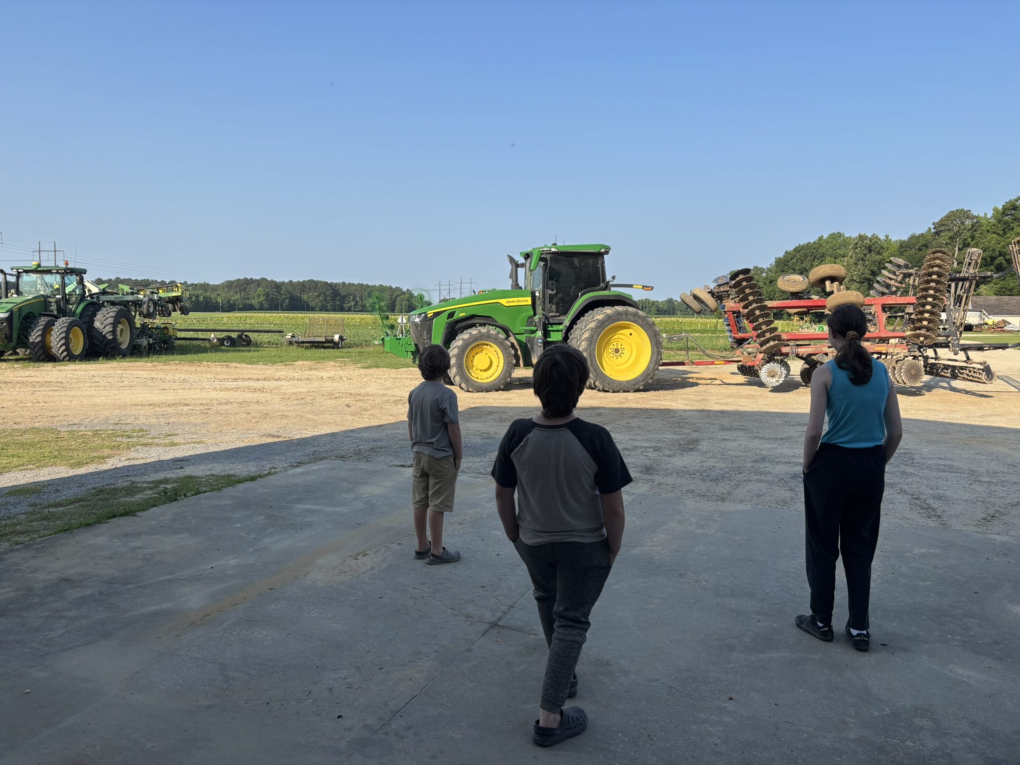 Three children observing large green tractors with cornfields and farm crops in the background at O’Neal Farms, Society Hill, SC